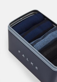 Caja de lata con cinco pares de calcetines FALKE. Los calcetines son de color marino, negro y un diseño a rayas azules, mezcla de algodón con textura acanalada.