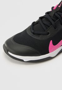 Black athletic shoe with breathable mesh upper, smooth black toe cap, pink Nike swoosh accent, and white sole. Laces and eyelets are black.