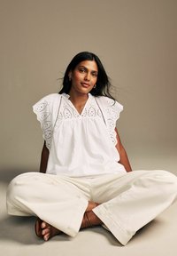 Blusa bianca in cotone con dettagli in pizzo, maniche a fisarmonica e vestibilità rilassata, abbinata a pantaloni a gamba larga color crema. Texture liscia.