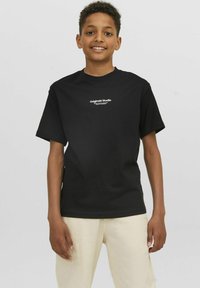 Camiseta de algodón negra con mangas cortas, que presenta un gráfico en blanco "Originals Studio" centrado en el pecho. Textura suave y corte relajado.