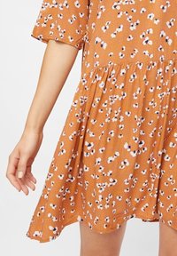 Vestito floreale arancione con fiori bianchi e neri. Maniche corte, vita arricciata e gonna svasata in un tessuto leggero e texturizzato.