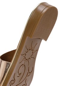 Sandalia de bronce metálico con una amplia suela marrón texturizada que presenta un patrón de sol. El tacón está ligeramente elevado y tiene un ribete dorado.