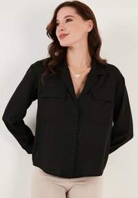 Camicia nera con bottoni, realizzata in tessuto morbido, con due tasche sul petto, un fit rilassato e maniche lunghe.