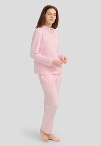 Conjunto de pijama rosa claro que incluye una camisa de manga larga con cuello abotonado y un suave patrón de lunares, combinado con pantalones a juego.