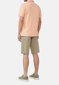 Różowa koszulka polo z kontrastowym kołnierzykiem, w połączeniu z jasnoniebieskimi szortami i szarymi sneakersami, widok od tyłu. Krótkie rękawy, luźny krój.