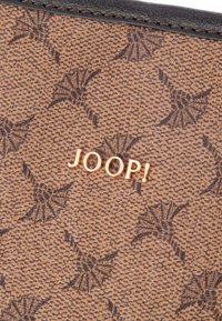 Materiale marrone con texture che presenta un motivo di stelle stilizzate; logo in rilievo "JOOP!" in metallo dorato. Cuciture scure lungo il bordo.