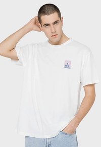 Biała bawełniana koszulka z niewielką pastelową grafiką i napisem "NAUTICA" na lewej piersi. Okrągły dekolt i krótkie rękawy.