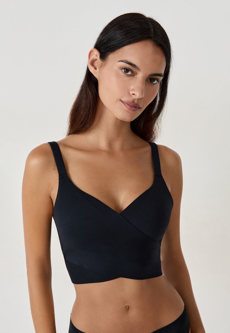 Zwarte naadloze bralette met een kruislings ontwerp, brede schouderbanden en een gladde textuur, met subtiele stikdetails.