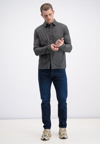 Szara, prążkowana koszula z długim rękawem, zapinana na guziki, noszona z ciemnoniebieskimi, dopasowanymi jeansami i beżowymi tenisówkami, na jednolitym tle.