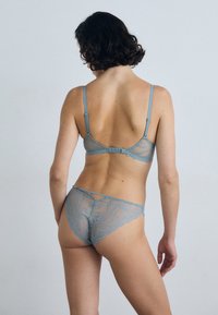 Kant lingerie set in zachtblauw, met delicate golvende patronen, dunne bandjes en een haak-en-oog sluiting aan de achterkant. De slip heeft vergelijkbare kantdetails.