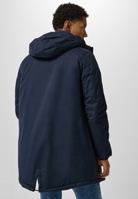 Parka azul marino con capucha, con una textura suave, diseño largo y una abertura en la parte trasera. Adecuada para climas más frescos.