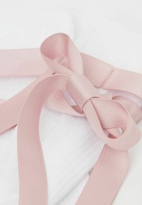 Tela blanca con una superficie texturizada, adornada con un lazo de cinta de satén de color rosa claro, que presenta un acabado suave y lazos en capas.