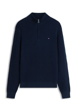 Marineblauwe gebreide trui met een halve rits bij de kraag, een textuur ribpatroon en een klein logo op de borst. Lange mouwen en geribbelde manchetten.