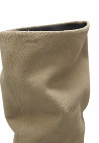 Beige suède laarzen met een slouchy ontwerp, voorzien van een gladde textuur en een gerolde bovenrand, met een reliëflogo aan de zijkant.