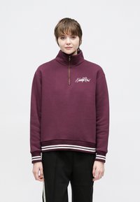 Bordeauxrode zip-up trui van een katoenmix, met een hoge kraag, witte gestreepte accenten aan de onderkant en geborduurd logo op de borst.