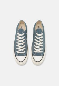 Blå canvas sneakers med hvite snører, gummitåhette og svart såletrim. Har kontraststing og metallhull.