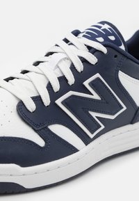 Námořnické a bílé syntetické kožené tenisky s bílými tkaničkami, polstrovaným límcem a velkým bílým logem "N" na boku. Hladké a texturované prvky.