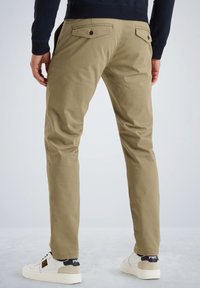 Kaki chinos s uskim krojem, koji imaju dva stražnja džepa, suptilnu teksturiranu tkaninu i čistu ivicu, upareni s bijelim tenisicama.