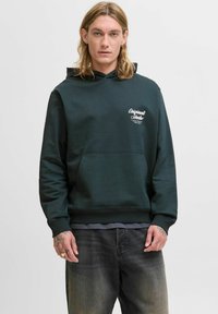 Sweatshirt à capuche vert foncé avec une poche kangourou, des poignets côtelés et un petit logo blanc sur la poitrine gauche. Tissu doux et texturé.