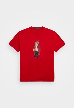 Rode T-shirt met korte mouwen met een teddybeer die een wintermuts, jas en geruite broek draagt, afgedrukt middenvoor.