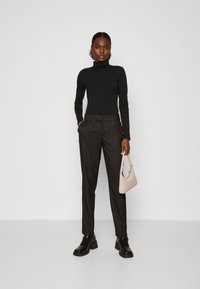 Svart turtleneck-top, svarta skräddarsydda byxor med pinstripes och svarta plattformsskor. Håller i en ljusbeige handväska med minimalistisk design.