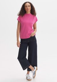 Roze T-shirt met korte mouwen en een hoge halslijn, gecombineerd met brede donkerdenim spijkerbroeken en grijze sneakers met blauwe accenten.