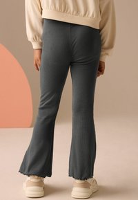 Graue, ausgestellte Ripp-Hosen mit rohem Saum, kombiniert mit cremefarbenen Sneakern. Die weiche Textur und das figurnahe Design betonen die Beine.