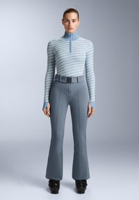 Ljusblå mönstrad långärmad topp med zipkrage, matchad med ljusgrå utsvängda byxor med bälte och sömdetaljer. Svarta stövlar fulländar looken.