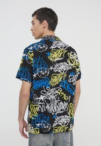 Camicia a maniche corte con base nera e motivi di graffiti multicolori in blu, giallo e bianco. Vestibilità casual con colletto.