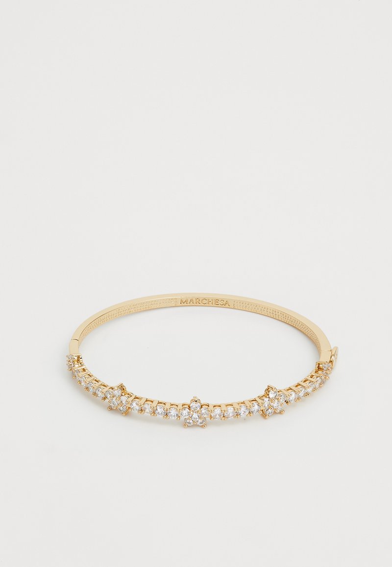 Brățară cu tonuri de aur având un design simetric, decorată cu pietre clare și strălucitoare, fixate într-o prindere cu colți, demonstrând măiestrie fină.