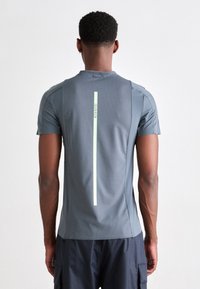 Vīrietis redzams no aizmugures, tērpts pelēkā īsajās piedurknēs sporta krekls ar vertikālu atstarojošu strīpu un uzrakstu "Calvin Klein" uz muguras.