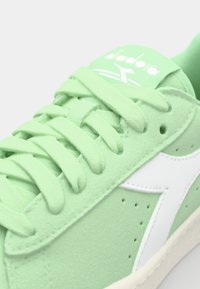 Sneaker verde in suede con logo e dettagli bianchi, dotata di lacci piatti, perforazioni sui lati e suola testurizzata.