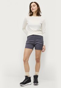 Lichte, langmouwcreme-top gecombineerd met donkergrijze shorts. Zwarte wandelschoenen met gestructureerde zolen en beige sokken maken de outfit compleet.