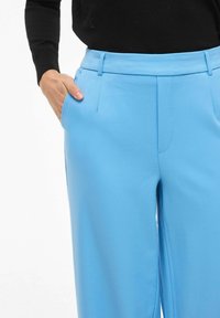 Lyseblå skræddersyede bukser i et glat stof med sidelomme, bæltestropper og flad front.