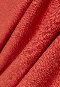 Strukturstoff in einem lebhaften Korallenton, mit weichen, leicht erhabenen Fasern, die ein warmes, einladendes Aussehen erzeugen.