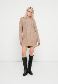 Knit sweater dress in light beige, featuring cable patterns and long sleeves, paired with black knee-high boots. Smooth texture, relaxed fit.