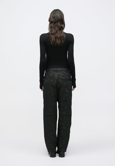 Μαύρο τοπ με μακριά μανίκια και εφαρμοστά μανίκια σε συνδυασμό με χαλαρό, υφασμάτινο μαύρο παντελόνι με σχέδιο και πλαϊνές τσέπες, φορεμένο με μαύρες μπότες.