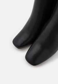 Black leather ankle boots featuring a smooth texture, square toes, and a fitted silhouette with no visible hardware or accents.