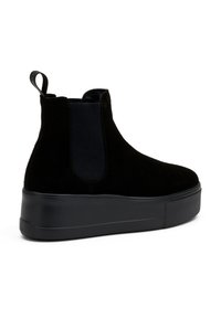 Botines de ante negro con paneles laterales elásticos, que presentan una suela de plataforma gruesa negra y una lengüeta en la parte posterior para facilitar su puesta.