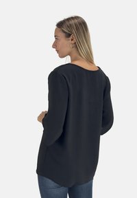 Zwarte top met lange mouwen, een ontspannen pasvorm, een zachte textuur en een ronde halslijn. Kenmerkend zijn de zijsplitten en de gebogen zoom.
