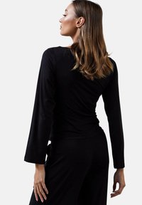 Czarny top z długim rękawem o dopasowanym kroju, miękkiej fakturze i okrągłym dekolcie, zestawiony z pasującymi spodniami, ukazujący prostą, elegancką sylwetkę.