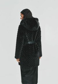 Czarny płaszcz z sztucznego futra z wzorem w zygzak, z kapturem i paskiem w talii. Projekt obejmuje długie rękawy i miękką teksturę.