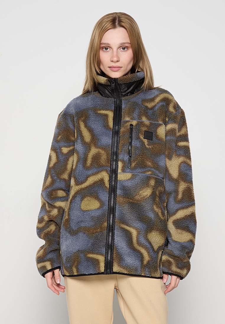 Veste en polaire avec un motif abstrait bleu, marron et beige, fermeture éclair à l'avant, col haut et une poche poitrine avec une fermeture éclair noire.
