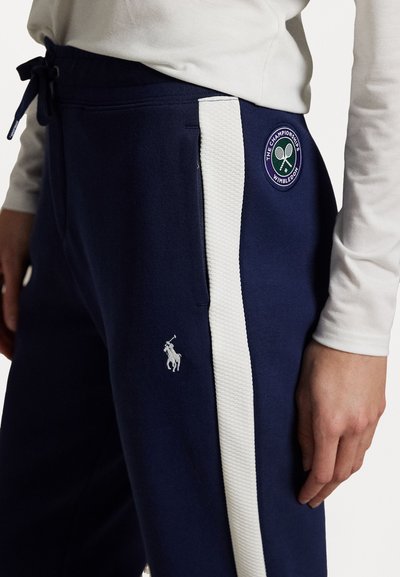 Tumed treeningpüksid valgete külgtriipudega, millel on tikandiga logo ja väike polo mängija embleem. Valmistatud pehmest, tekstuuriga kangast.