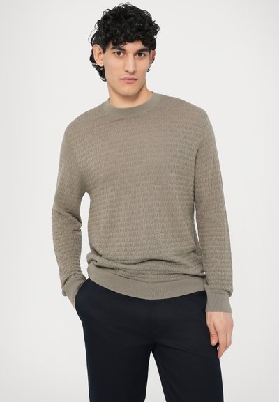 Svetlozelený sveter s textúrovaným pleteným vzorom s opakujúcimi sa písmenami. Okrúhly výstrih a rebrované manžety, doplnený o tmavé nohavice.