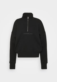 Sudadera negra recortada con cuello alto y cierre de cremallera. Presenta el logo bordado "CALVIN KLEIN JEANS" en hilo a juego. Material suave.