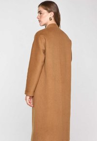 Cappotto di lana marrone con una vestibilità su misura, caratterizzato da una silhouette dritta, maniche lunghe e un design pulito e minimalista.