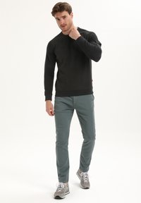 Zwarte crewneck sweatshirt, grijze slim-fit broek en grijze sneakers. Het materiaal lijkt zacht met ribgebreide manchetten. Casual outfit met een relaxte pasvorm.