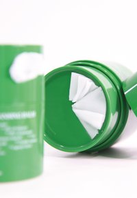 Zielony okrągły pojemnik z białą pokrywką, zawierający złożone białe podkładki oczyszczające wewnątrz, o gładkiej teksturze i prostym wzornictwie.