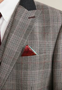 Blazer grigio a scacchi con colletto nero; presenta un fazzoletto da taschino rosso e turchese. Tessuto testurizzato, con pattern e colori a contrasto.